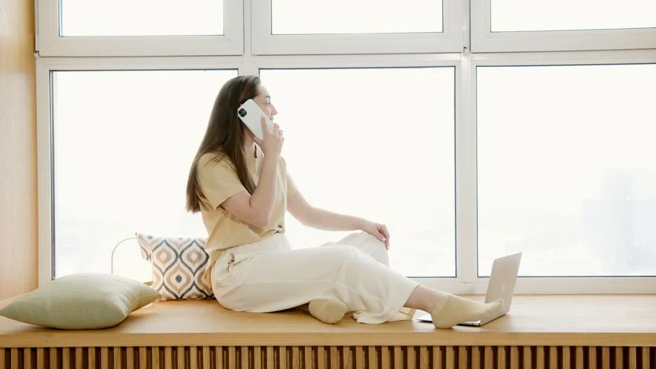 Femme assise près d’une fenêtre qui parle au téléphone